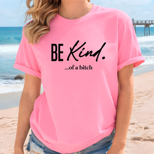 Woman wearing a pink t-shirt with 'BE KIND...of a bitch' text on a beach.