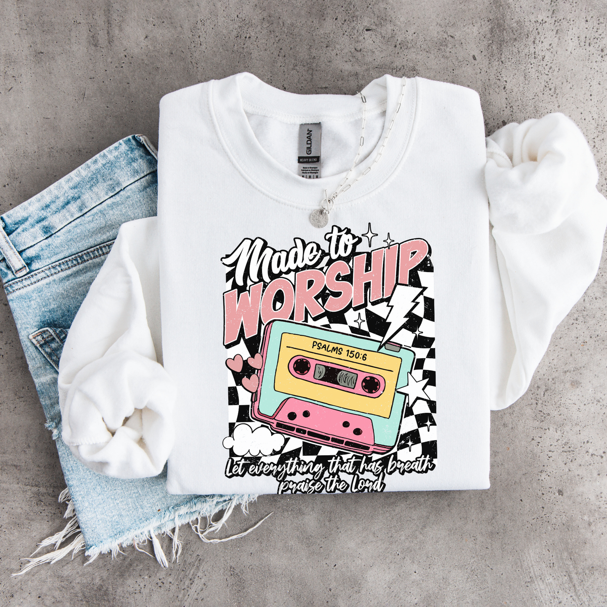 White Made to Worship crewneck sweatshirt flat lay with a retro cassette graphic, styled with denim.