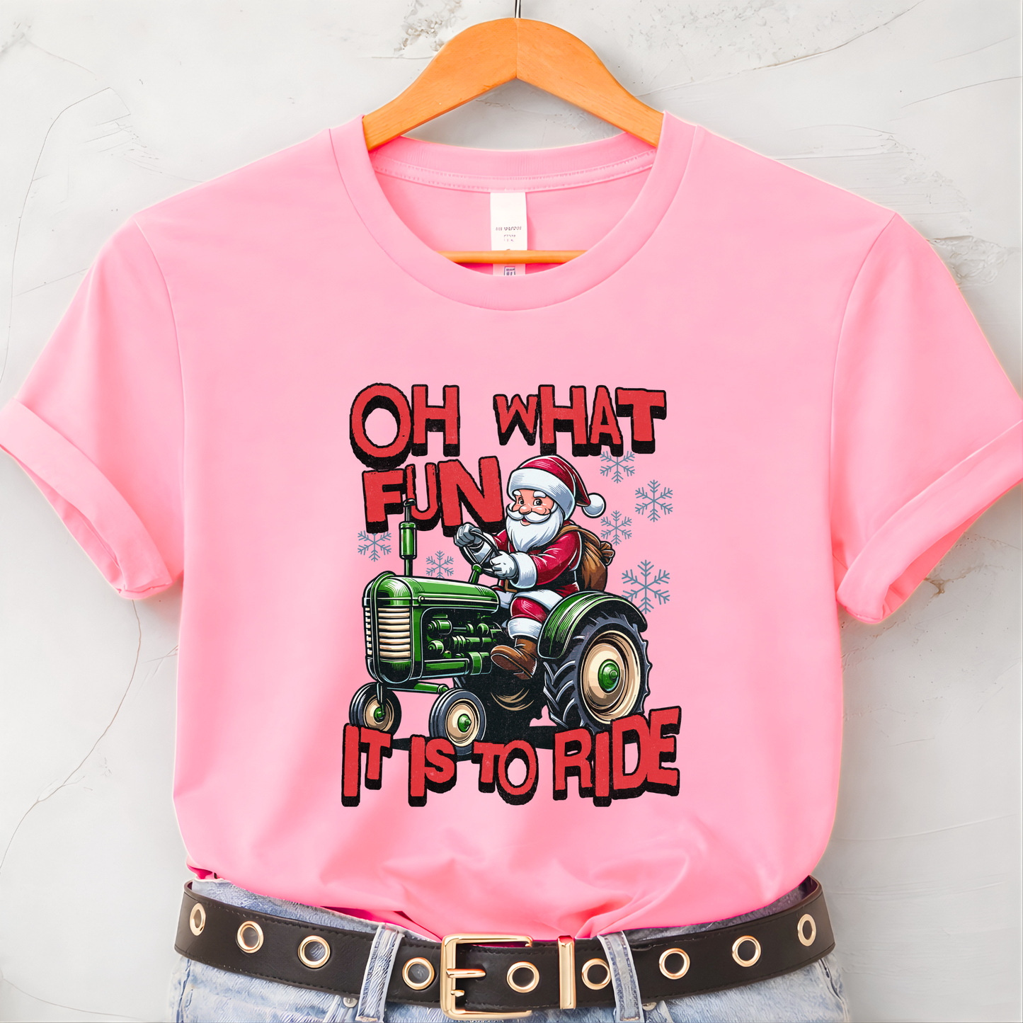 Pink t-shirt with Santa driving a tractor graphic and text on a hanger.