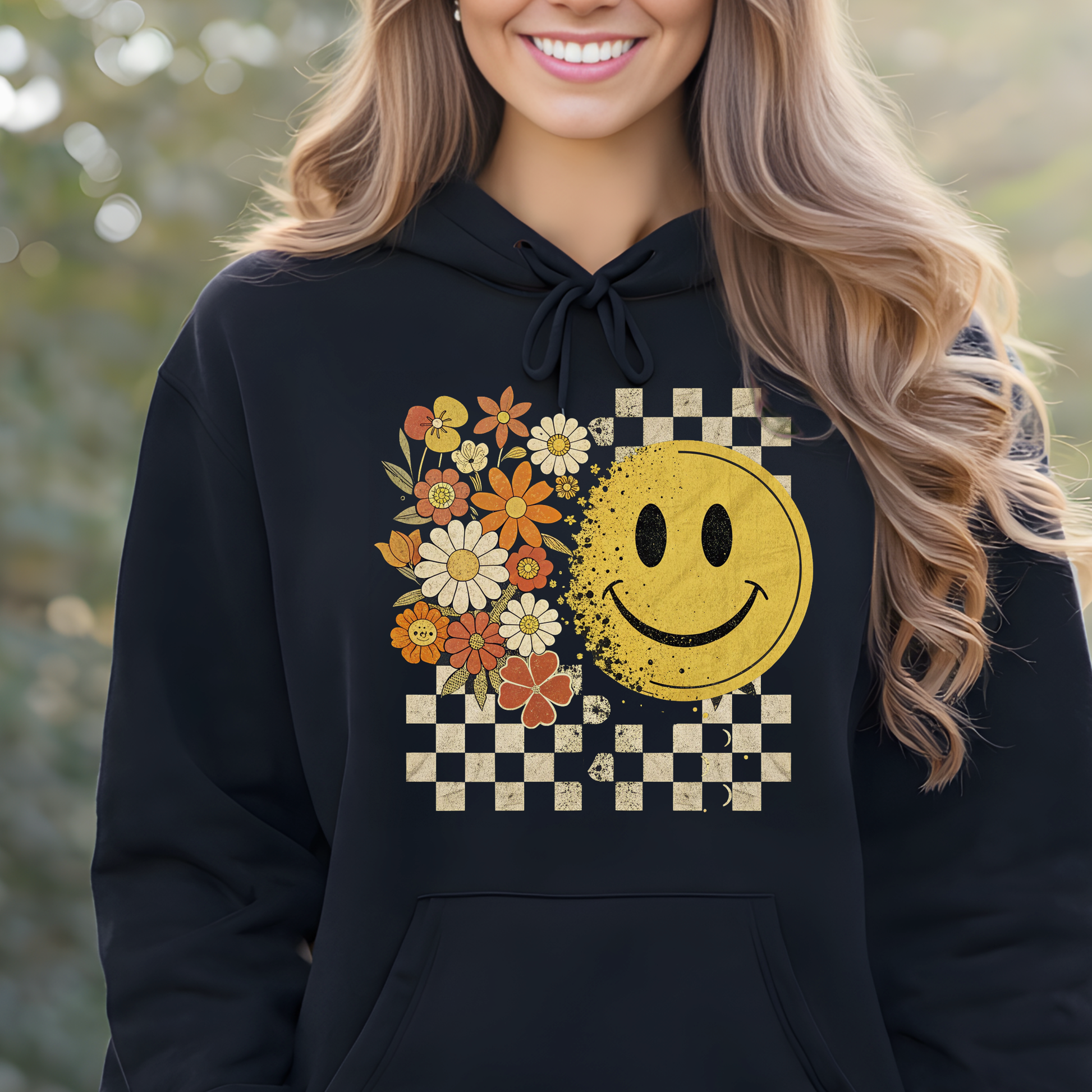 Woman wearing a black retro hoodie with a smiley face and floral design, standing outdoors.