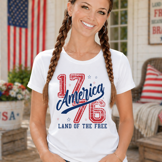 Woman wearing a white t-shirt with '1776 America Land of the Free' design, standing outdoors.