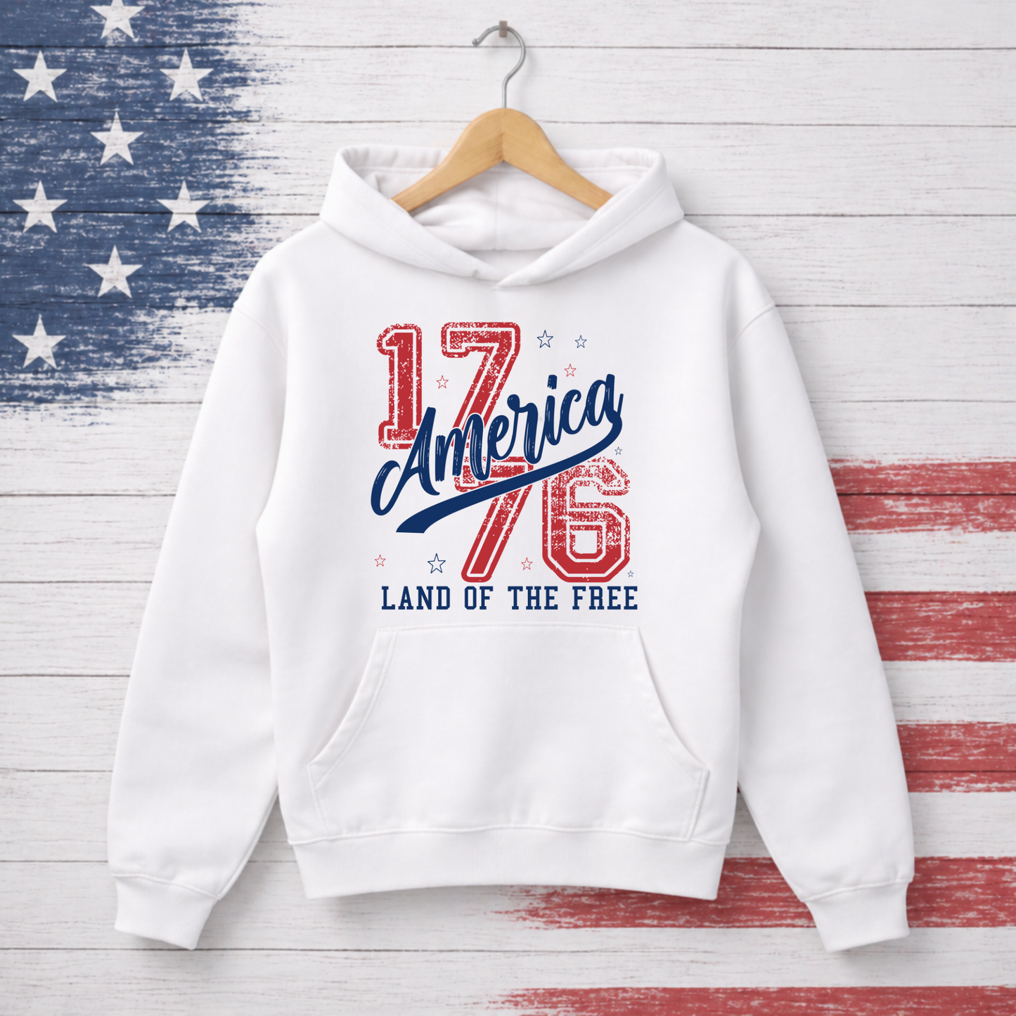 White hoodie with '1776 America Land of the Free' text on a wooden background with American flag pattern