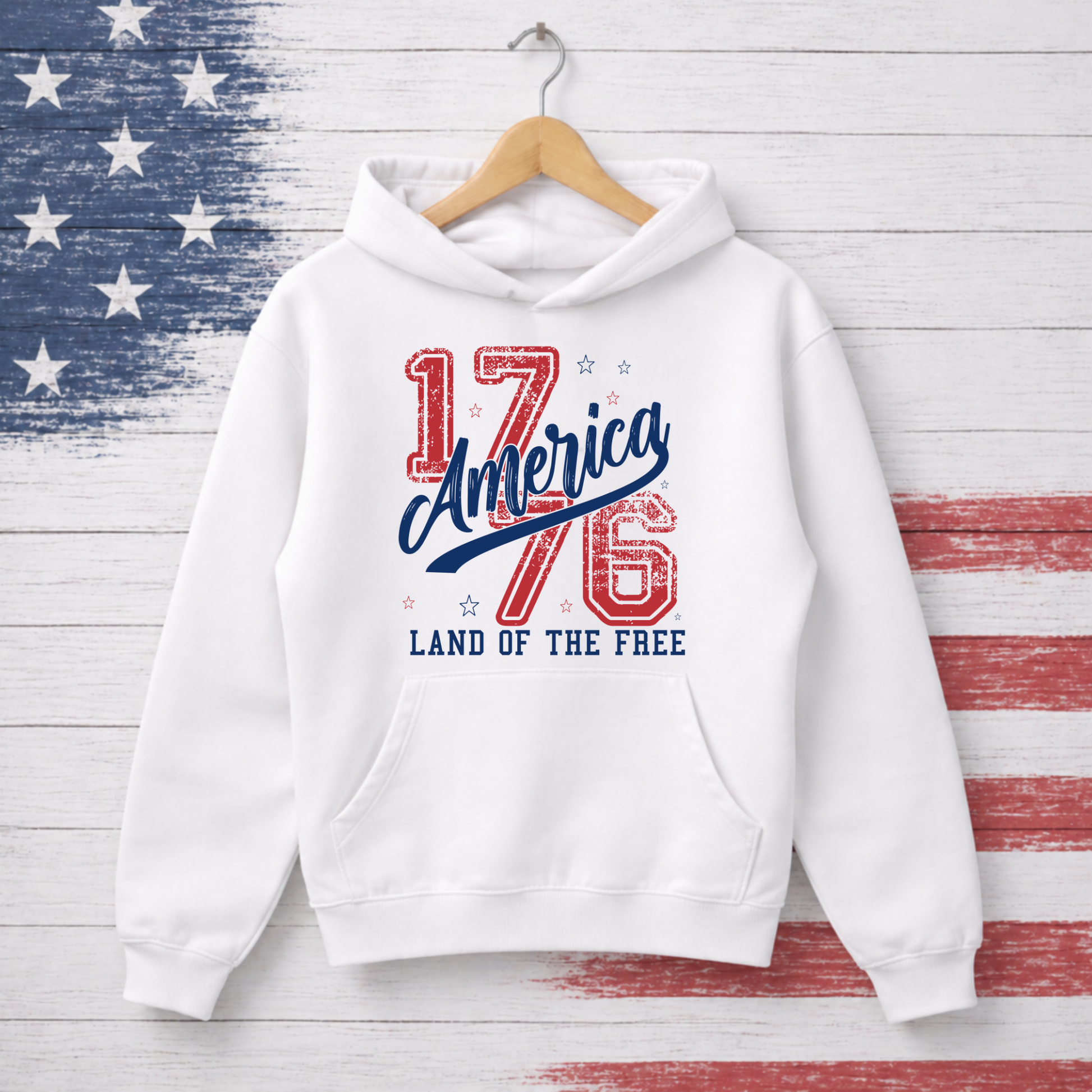 White hoodie with '1776 America Land of the Free' text on a wooden background with American flag pattern