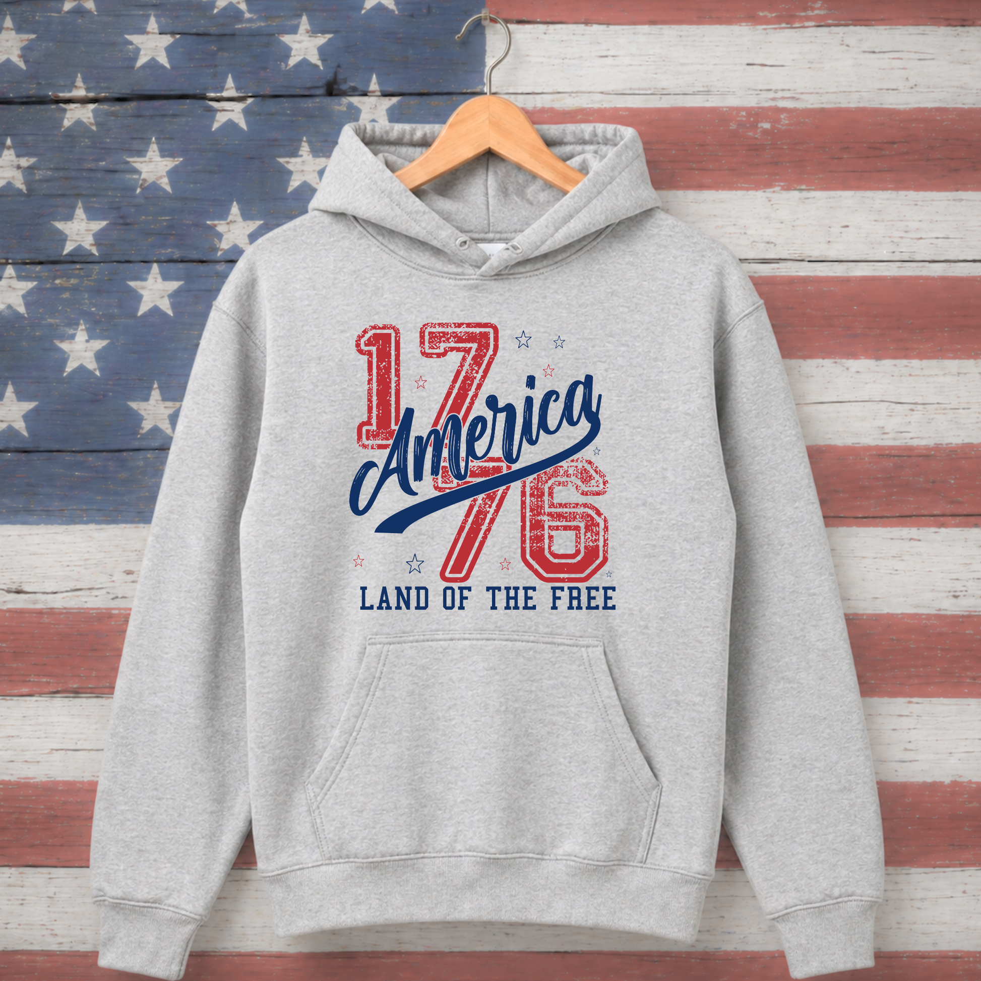 Gray hoodie with '1776 America Land of the Free' text on a wooden American flag background