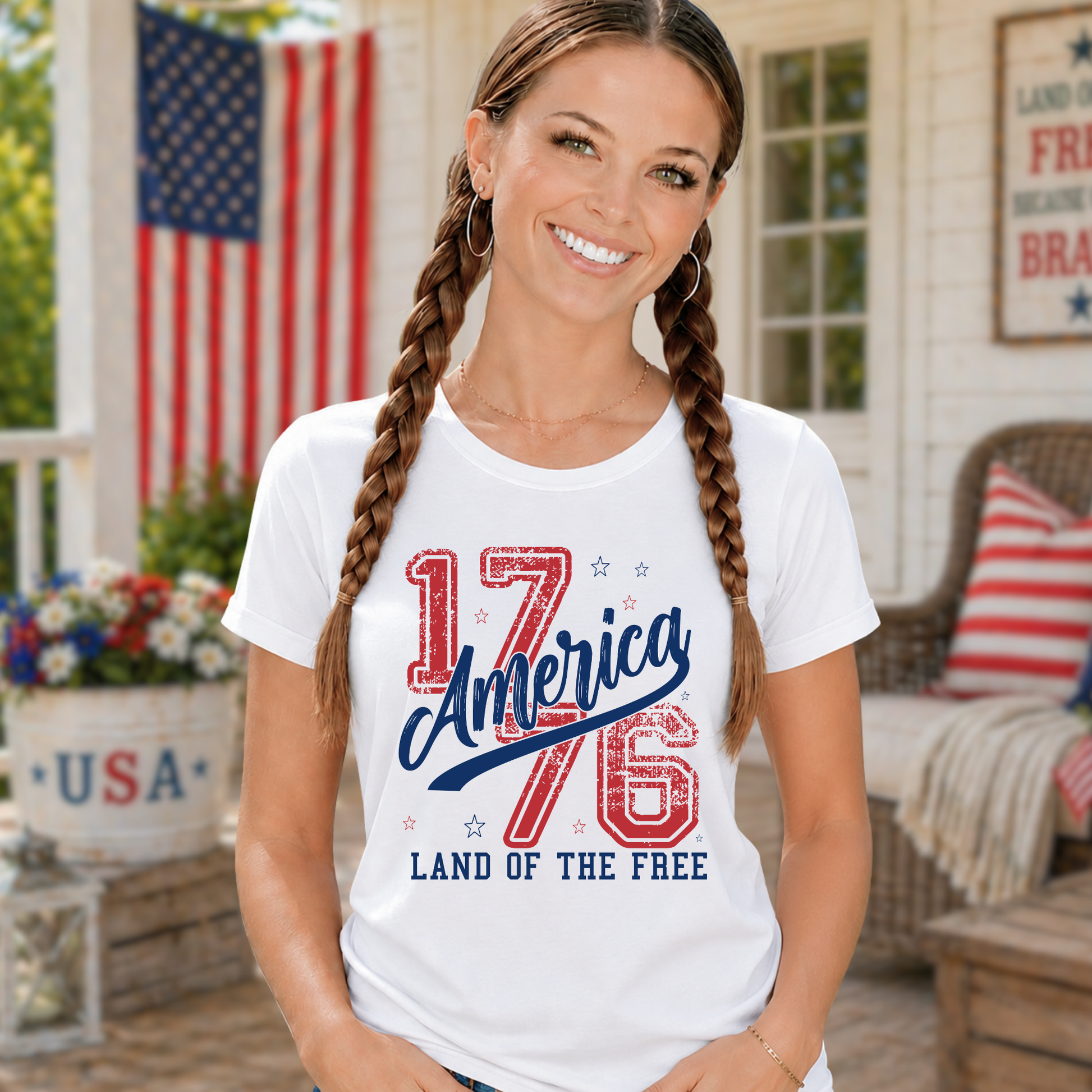 Woman wearing a white t-shirt with '1776 America Land of the Free' design on a porch with an American flag in the background.