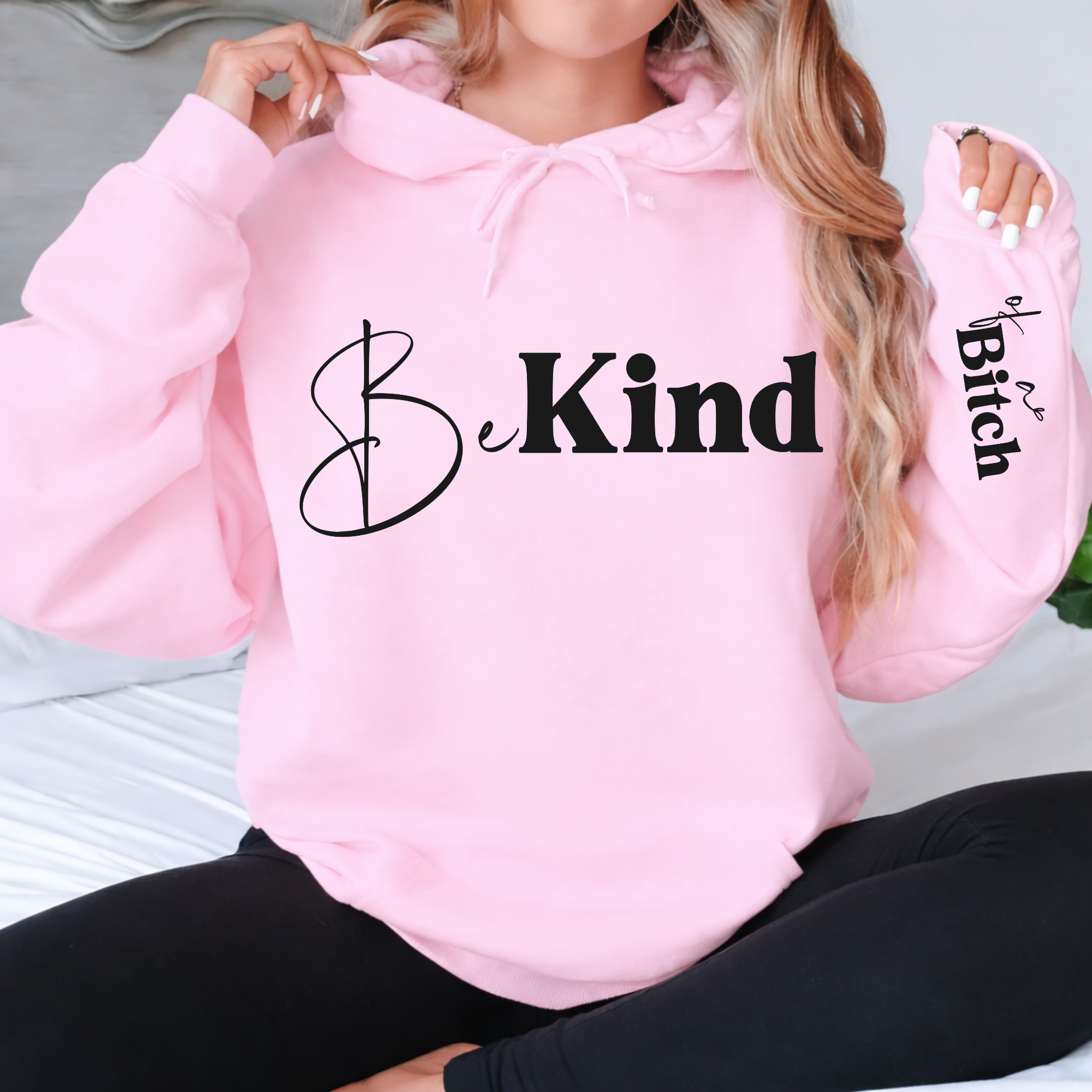 Pink hoodie with 'Be Kind' text on a person sitting.