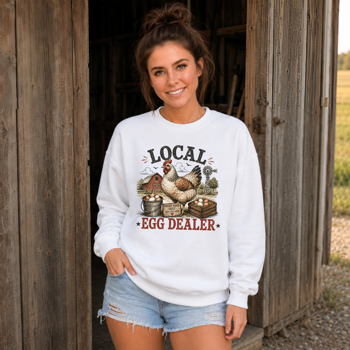 Woman in a white Local Egg Dealer sweatshirt at a rustic barn entrance.