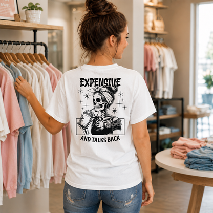 Woman showing the back of a white T-shirt with a black Expensive and Talks Back skeleton-woman graphic in a boutique.