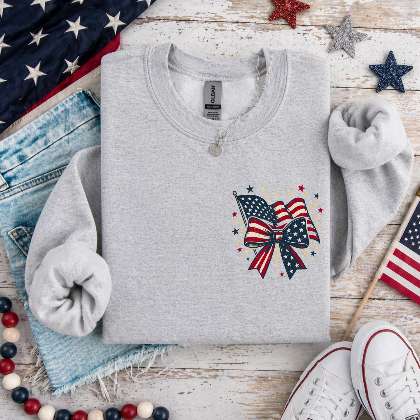 Gray sweatshirt with a patriotic design on a wooden surface with American flags and jeans.