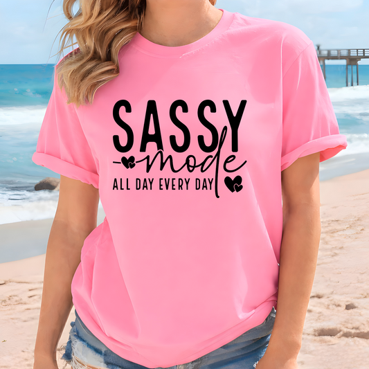 Woman wearing a pink t-shirt with 'Sassy Mode All Day Every Day' text on a beach.