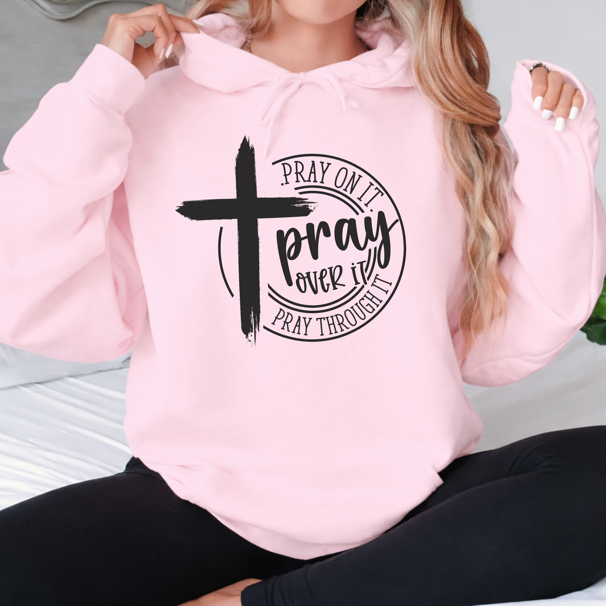 Person wearing a pink hoodie with a black cross and text design.