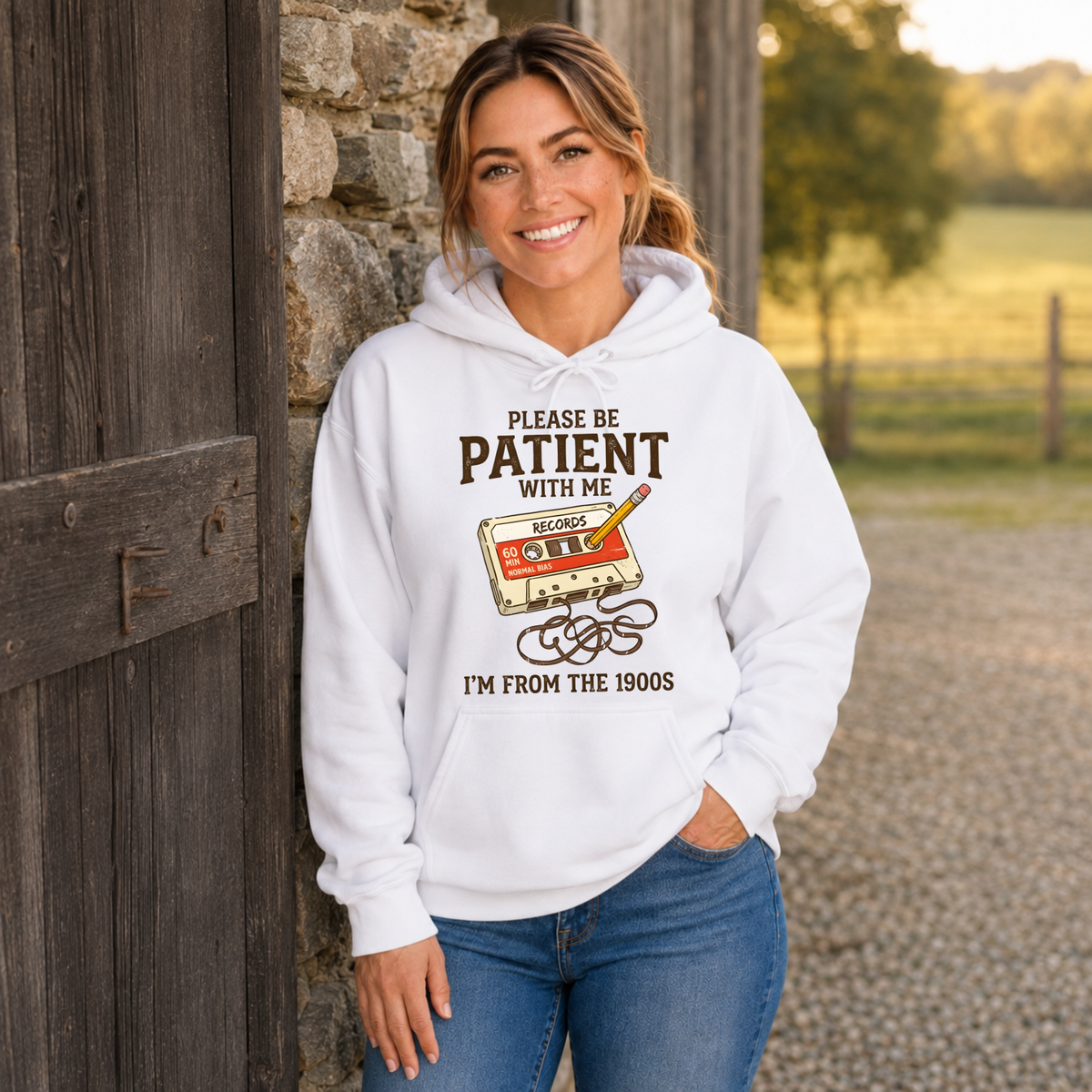 Woman wearing a white hoodie with a cassette tape and pencil graphic reading Please Be Patient With Me, I’m From the 1900s.