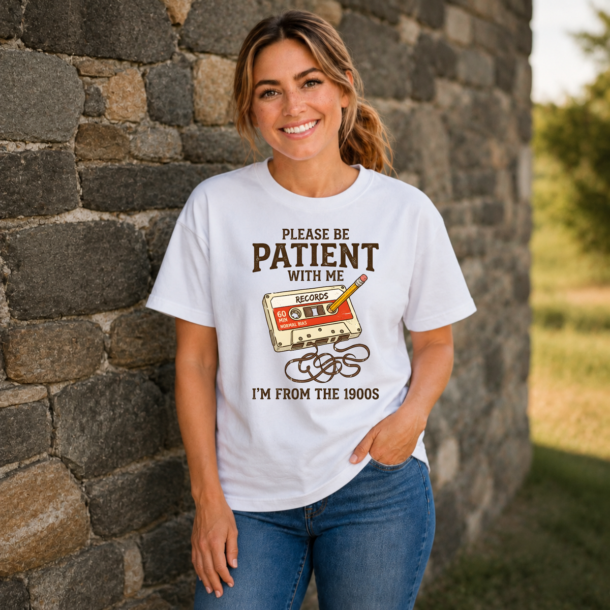 Woman wearing a white T-shirt with a cassette tape and pencil graphic reading Please Be Patient With Me, I’m From the 1900s.