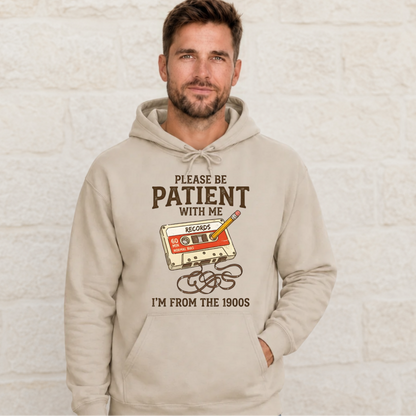 Man wearing a sand hoodie with the Please Be Patient With Me, I’m From the 1900s cassette tape and pencil graphic.