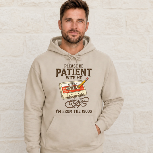 Man wearing a sand hoodie with the Please Be Patient With Me, I’m From the 1900s cassette tape and pencil graphic.