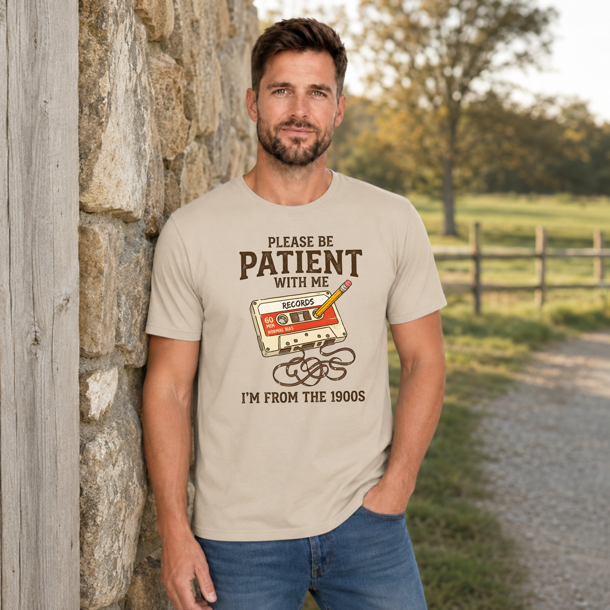 Man wearing a sand T-shirt with a cassette tape graphic reading Please Be Patient With Me, I’m From the 1900s.