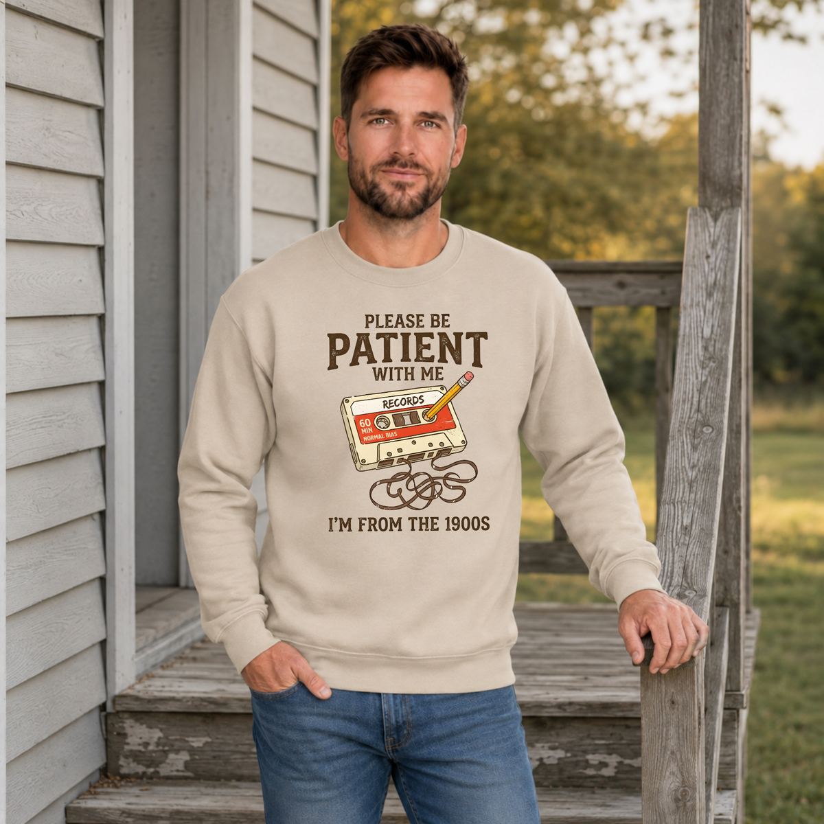 Man wearing a sand crewneck sweatshirt with a cassette tape and Please Be Patient With Me, I’m From the 1900s text.