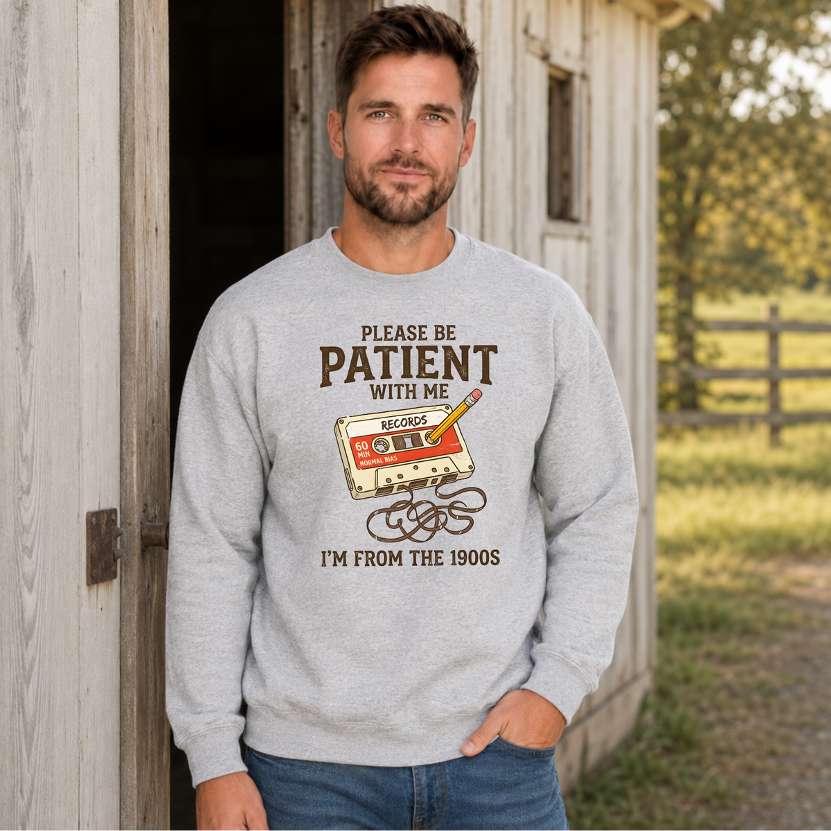 Man wearing a sports gray crewneck sweatshirt featuring the Please Be Patient With Me, I’m From the 1900s cassette tape design.