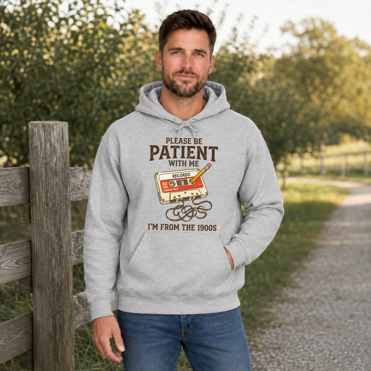Man wearing a sports gray hoodie with a cassette tape and pencil graphic reading Please Be Patient With Me, I’m From the 1900s.