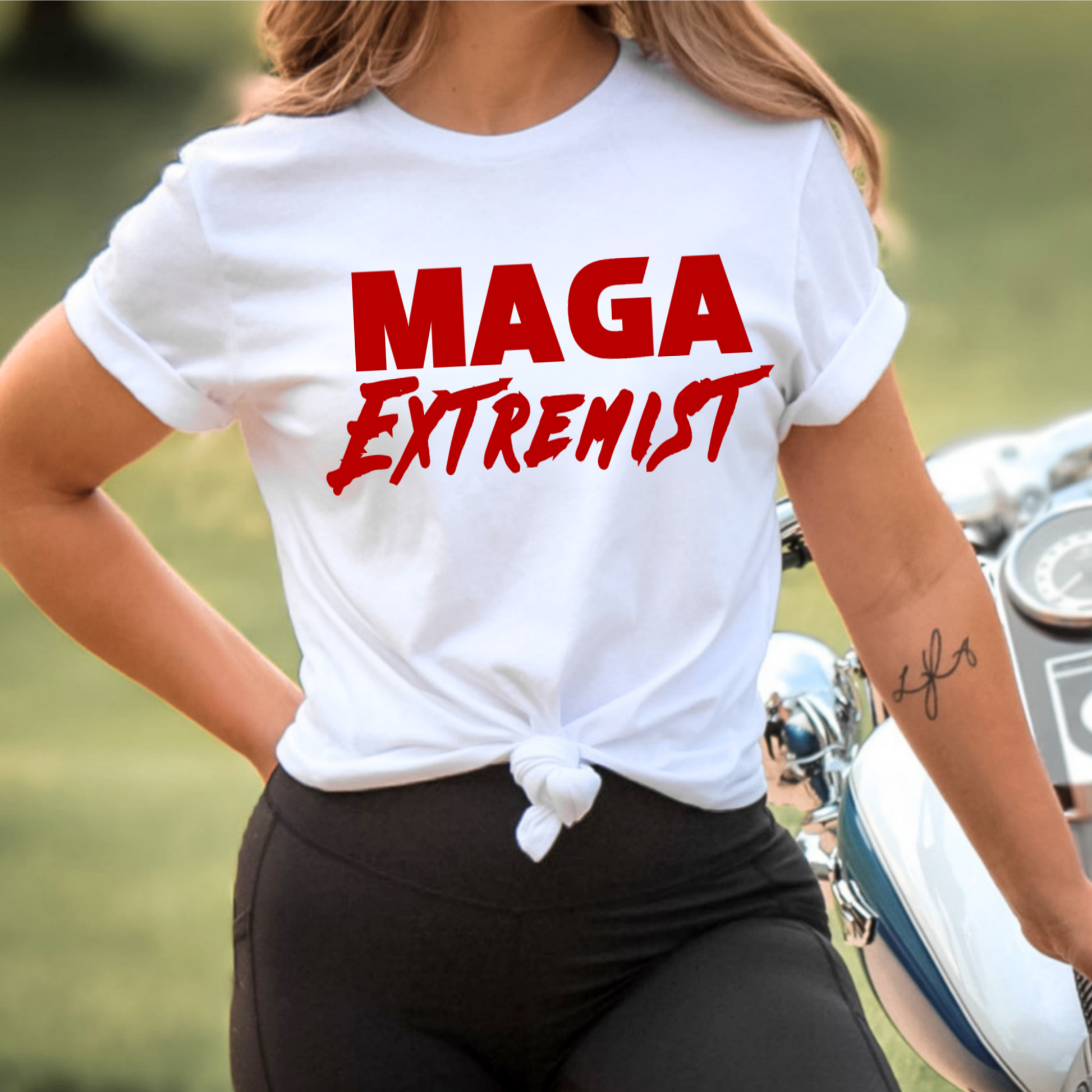 Person wearing a white t-shirt with 'MAGA Extremist' text in red, standing next to a motorcycle.