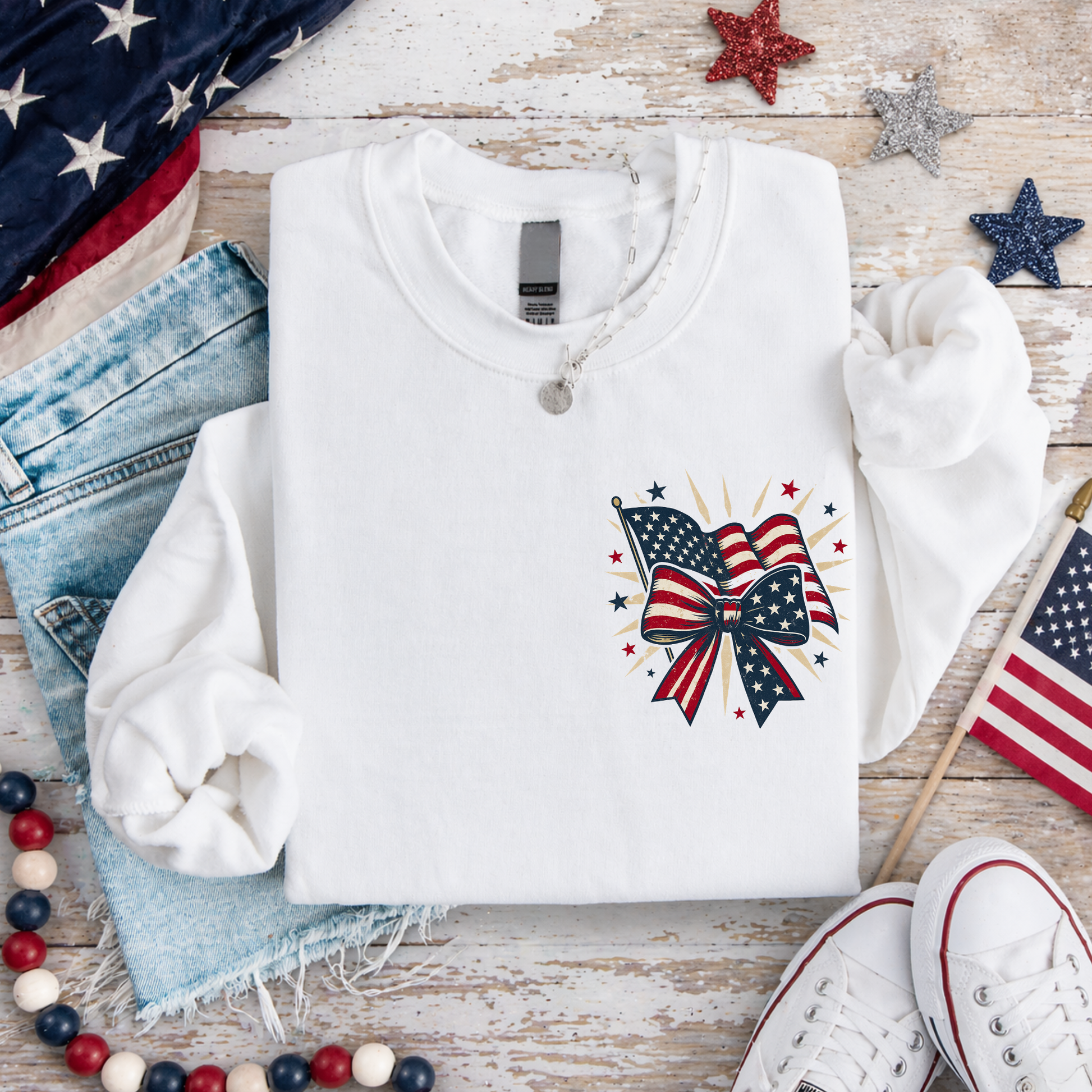 White sweatshirt with American flag design on a wooden surface with decorative items.