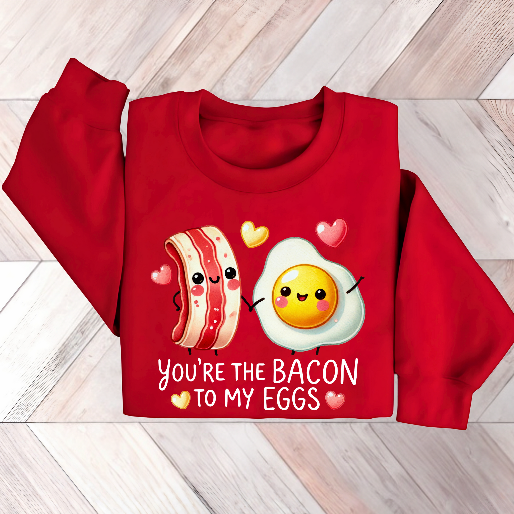 Flat lay of a red sweatshirt with a cute bacon and egg holding hands and colorful hearts, captioned “You're the Bacon to My Eggs.”