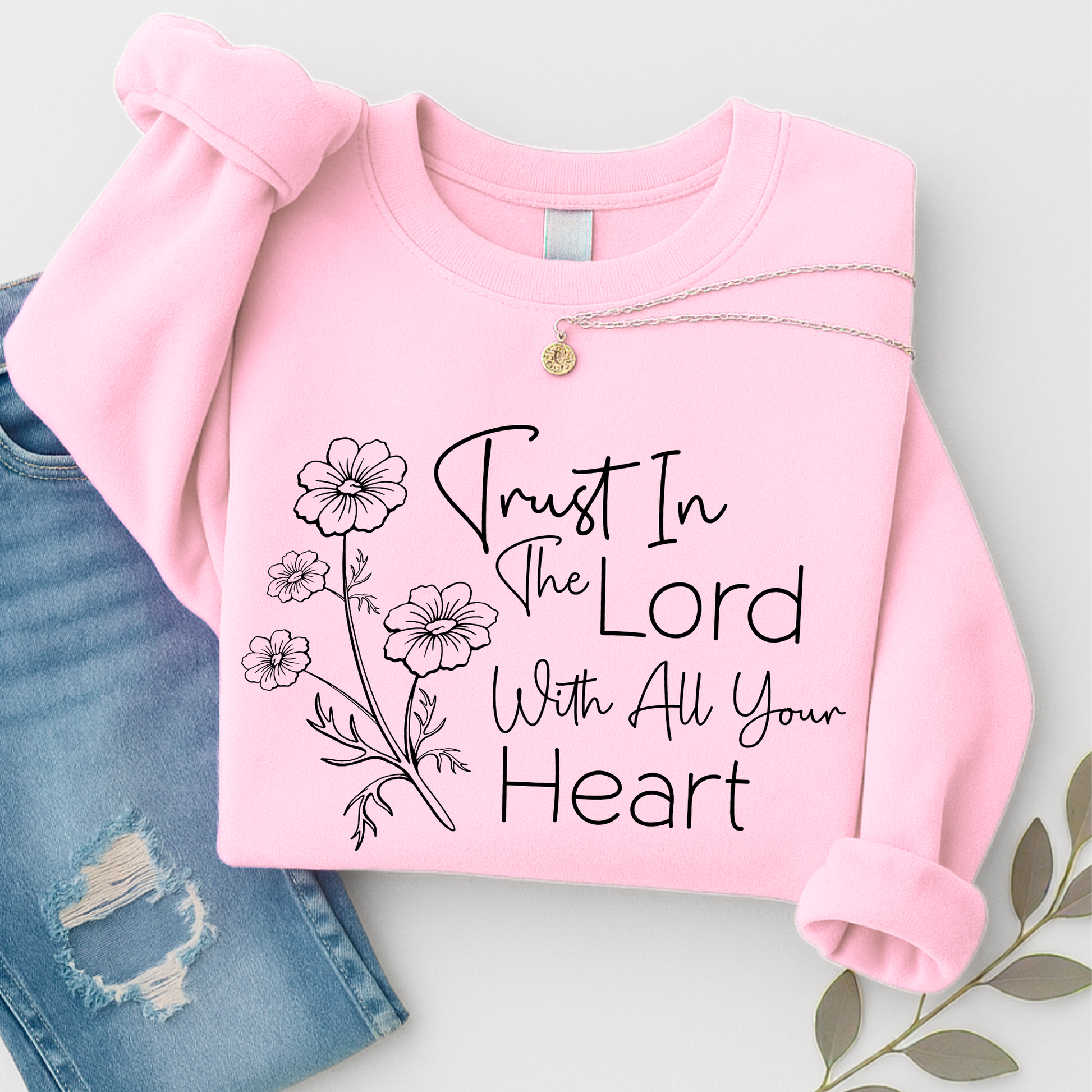 Pink sweatshirt with 'Trust In The Lord With All Your Heart' text and floral design on a light gray background.
