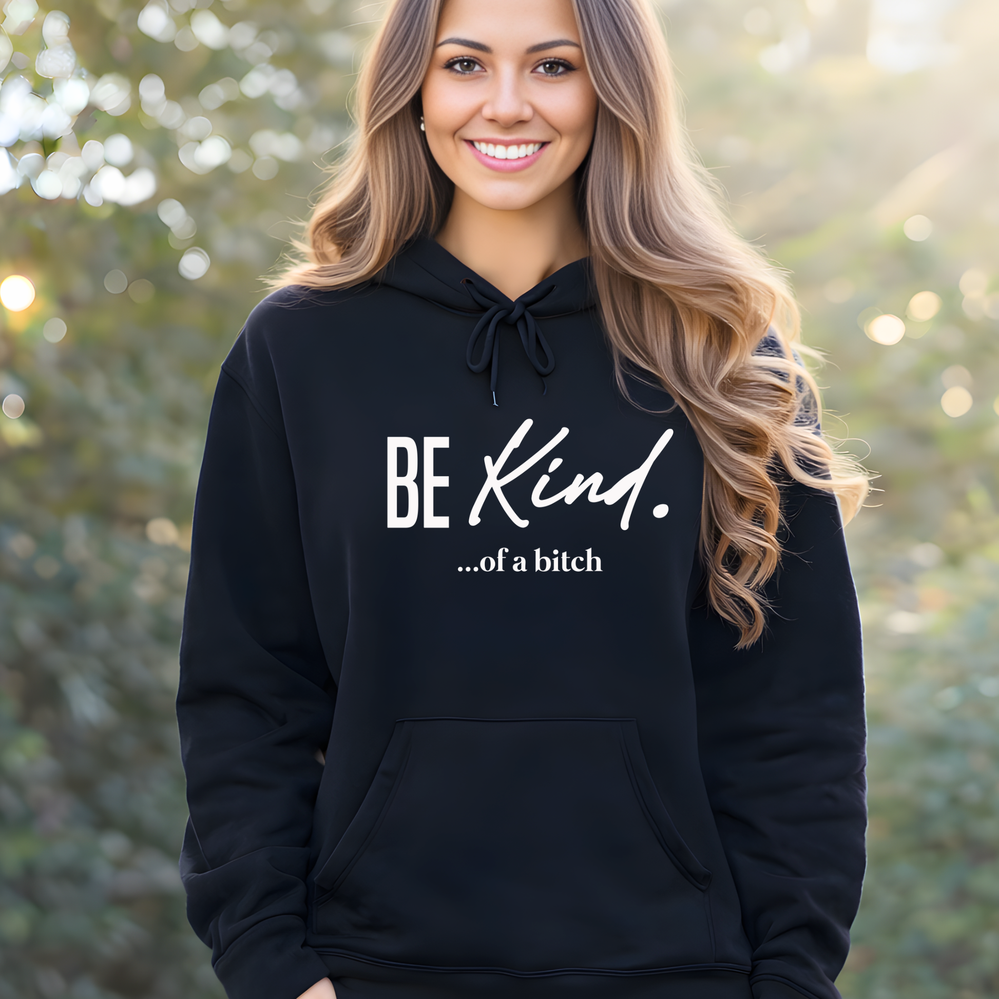 Woman wearing a black hoodie with 'BE KIND...of a bitch' text outdoors.