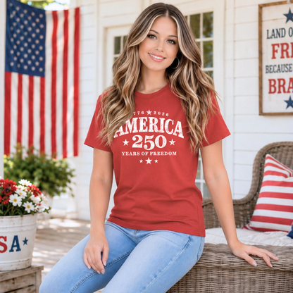 Woman wearing a red t-shirt with 'America 250' text, sitting on a porch with an American flag in the background.