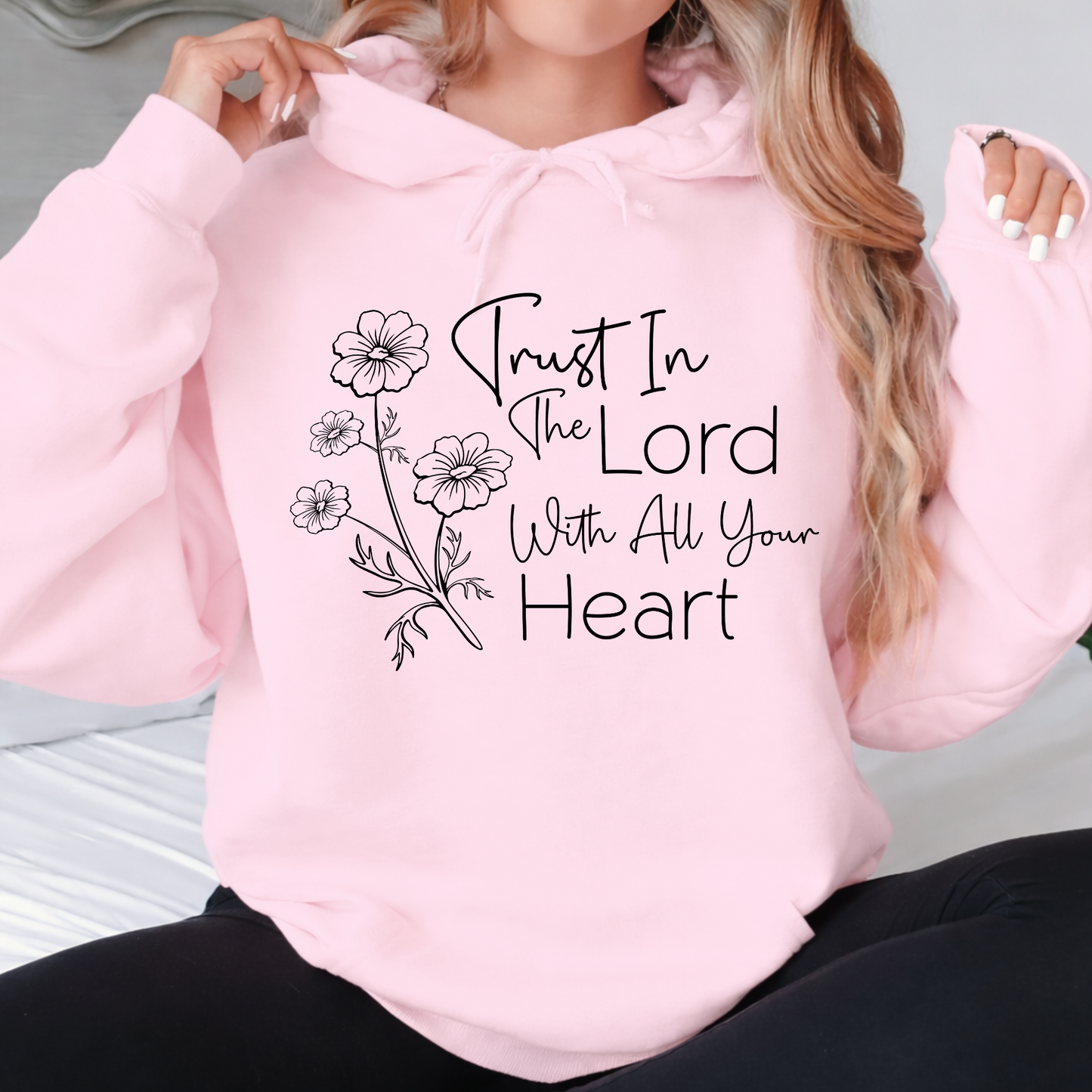 Pink hoodie with floral design and text 'Trust In The Lord With All Your Heart' worn by a person.