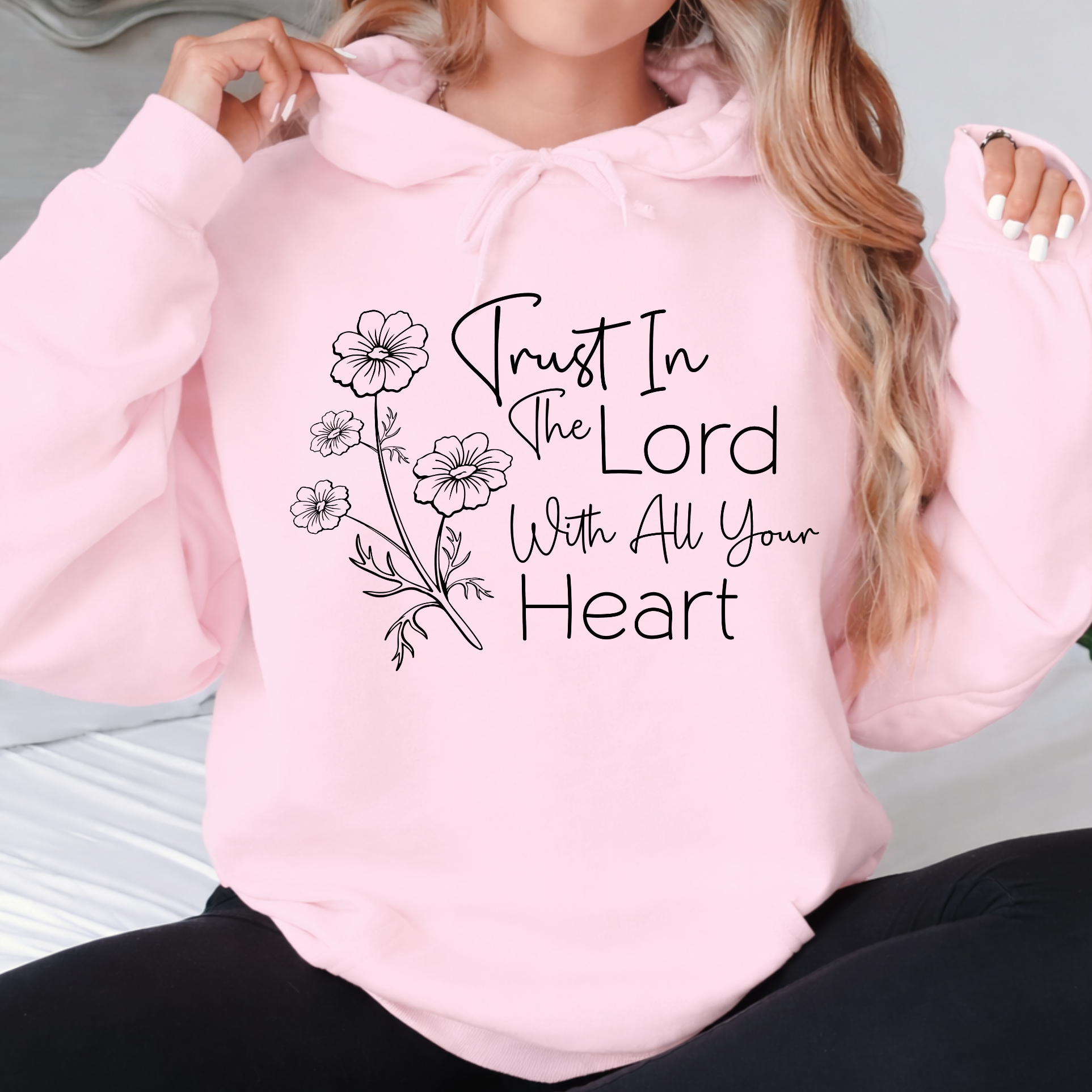 Pink hoodie with floral design and text 'Trust In The Lord With All Your Heart' worn by a person.