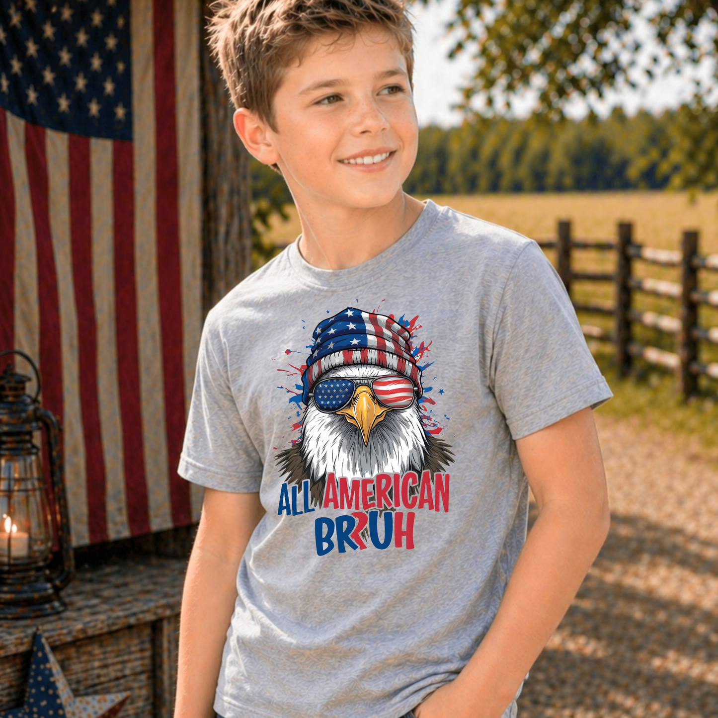 Child wearing a gray t-shirt with an eagle graphic and 'All American Bruh' text, standing outdoors with an American flag in the background.
