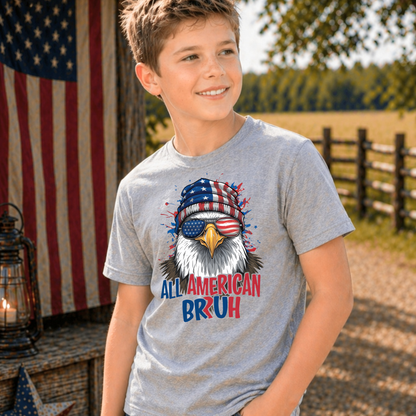 Child wearing a gray t-shirt with an eagle graphic and 'All American Bruh' text, standing outdoors with an American flag in the background.