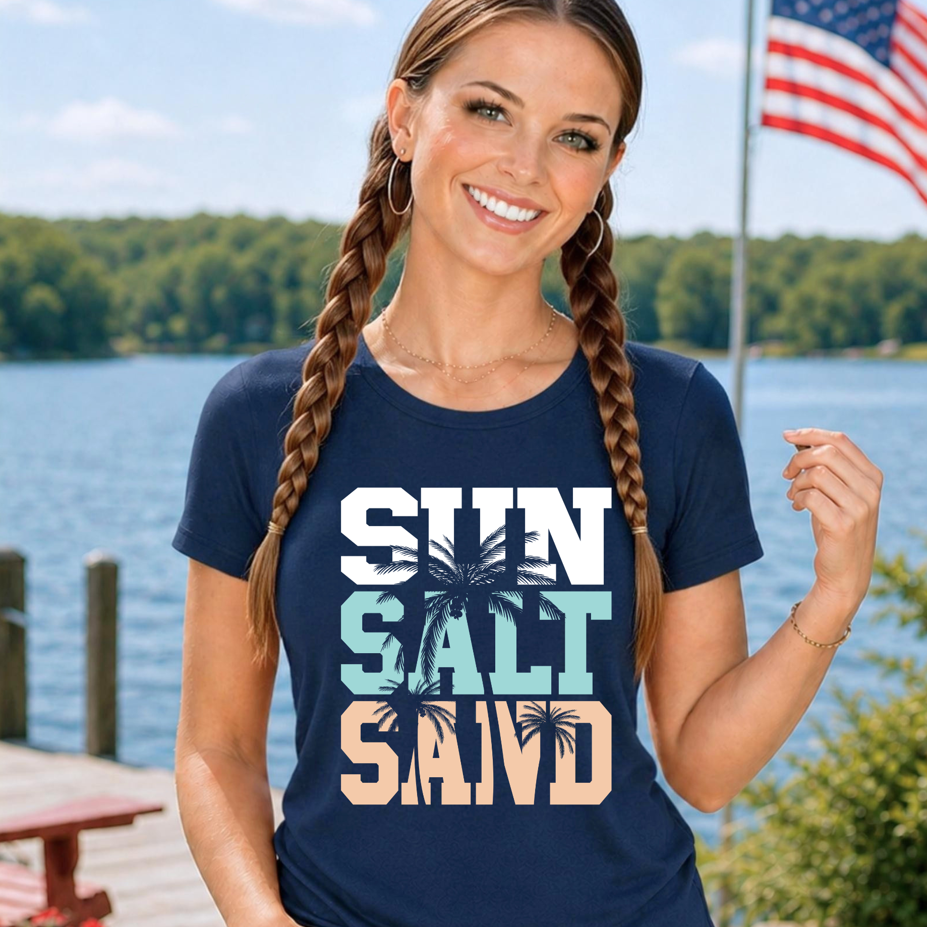 Woman wearing a navy blue t-shirt with 'Sun Salt Sea' design by a lake with an American flag in the background.
