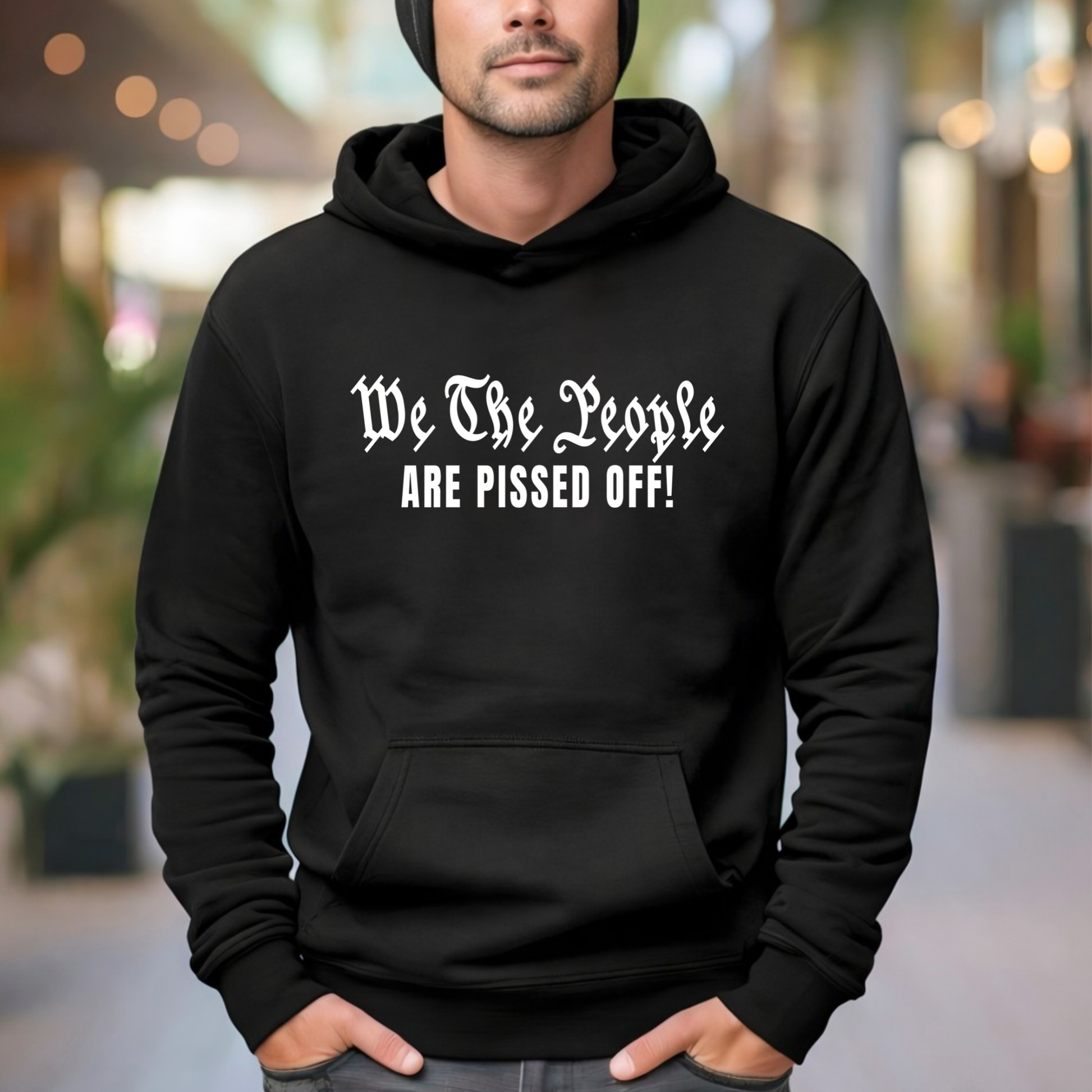 A Man wearing a black hoodie with text 'We The People ARE PISSED OFF!' in an outdoor setting.