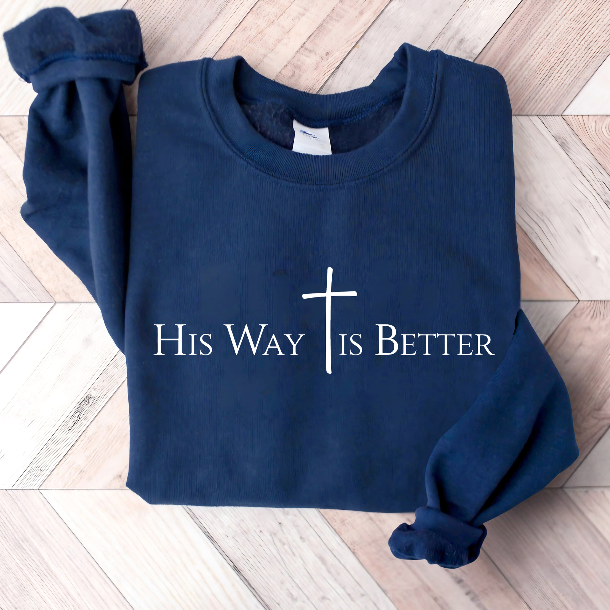 Navy blue sweatshirt with 'His Way Is Better' text and cross on a wooden floor.