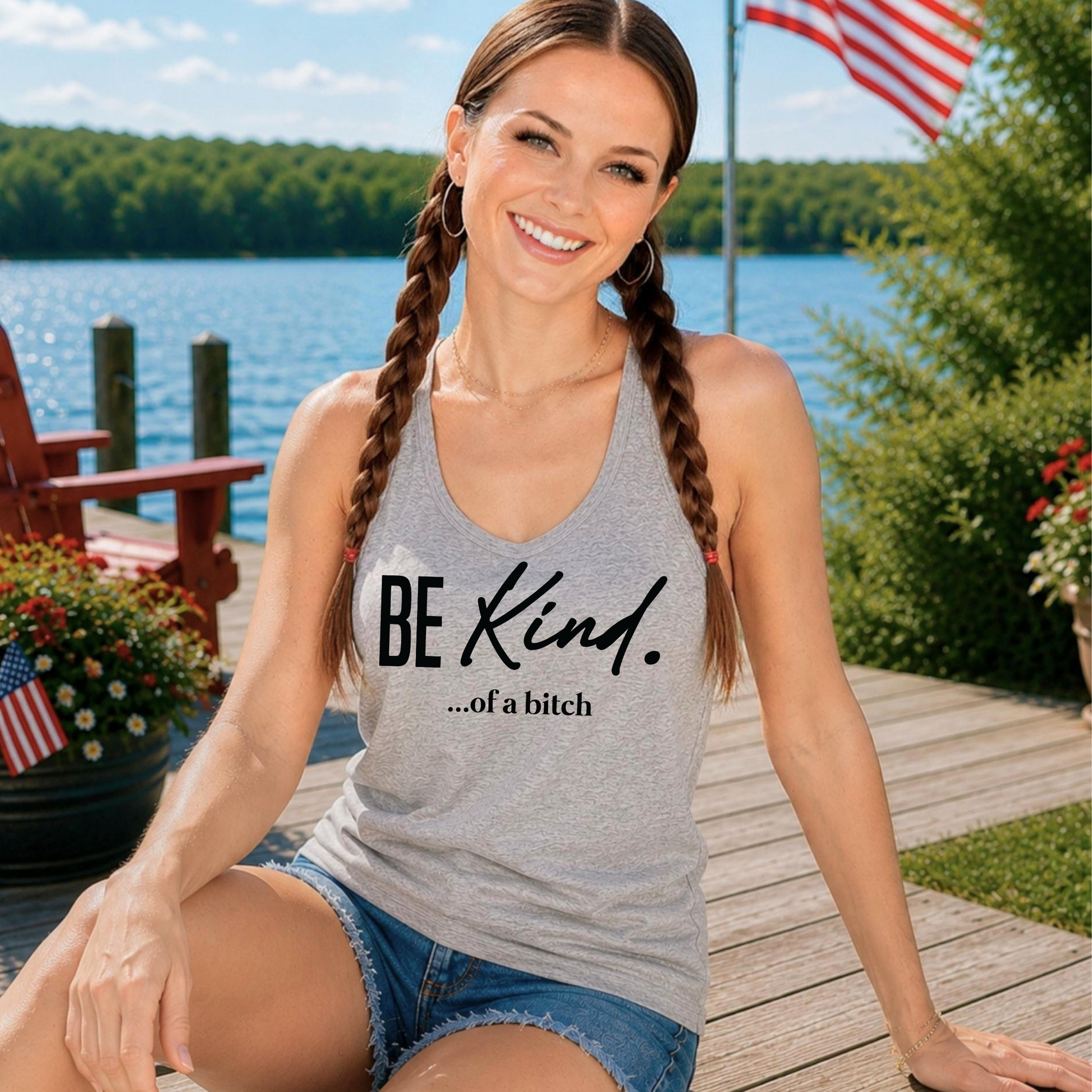 Woman wearing a tank top with 'BE Kind...of a bitch' text by a lake.