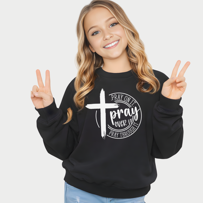 Young girl wearing a black sweatshirt with a cross and text design, making peace signs.