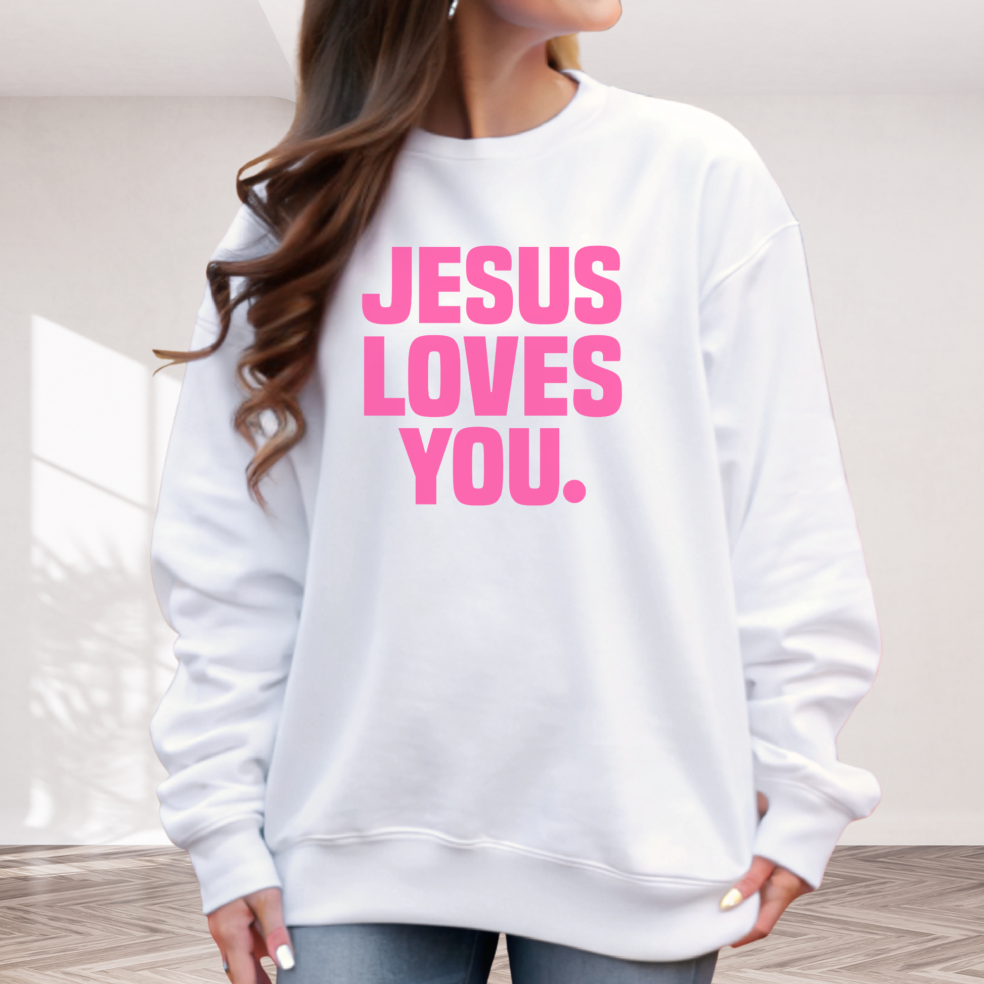 White sweatshirt with 'Jesus Loves You' text in pink on a neutral background