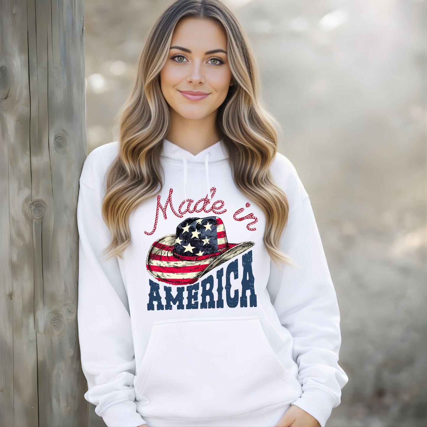 Woman wearing a white hoodie with 'Made in America' design, standing against a wooden fence.