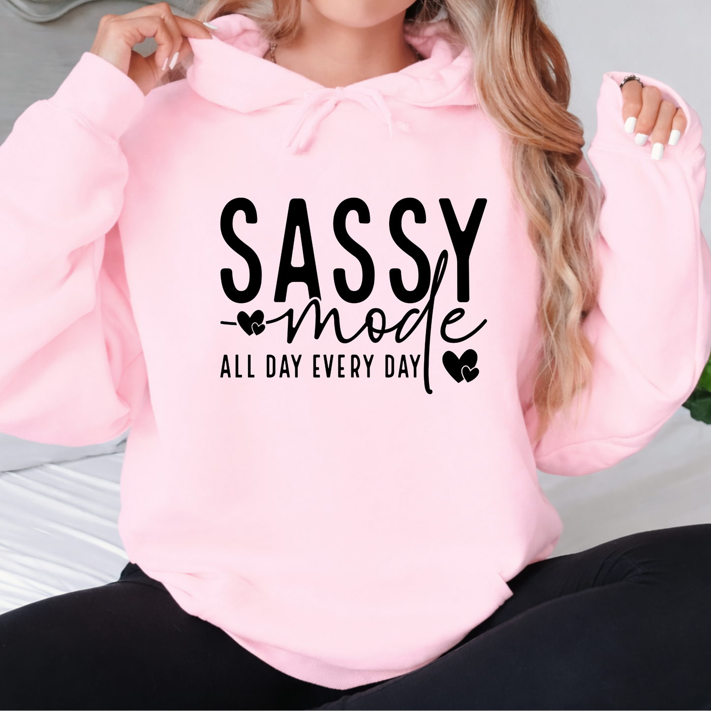 Pink hoodie with 'Sassy mode all day every day' text worn by a Woman .