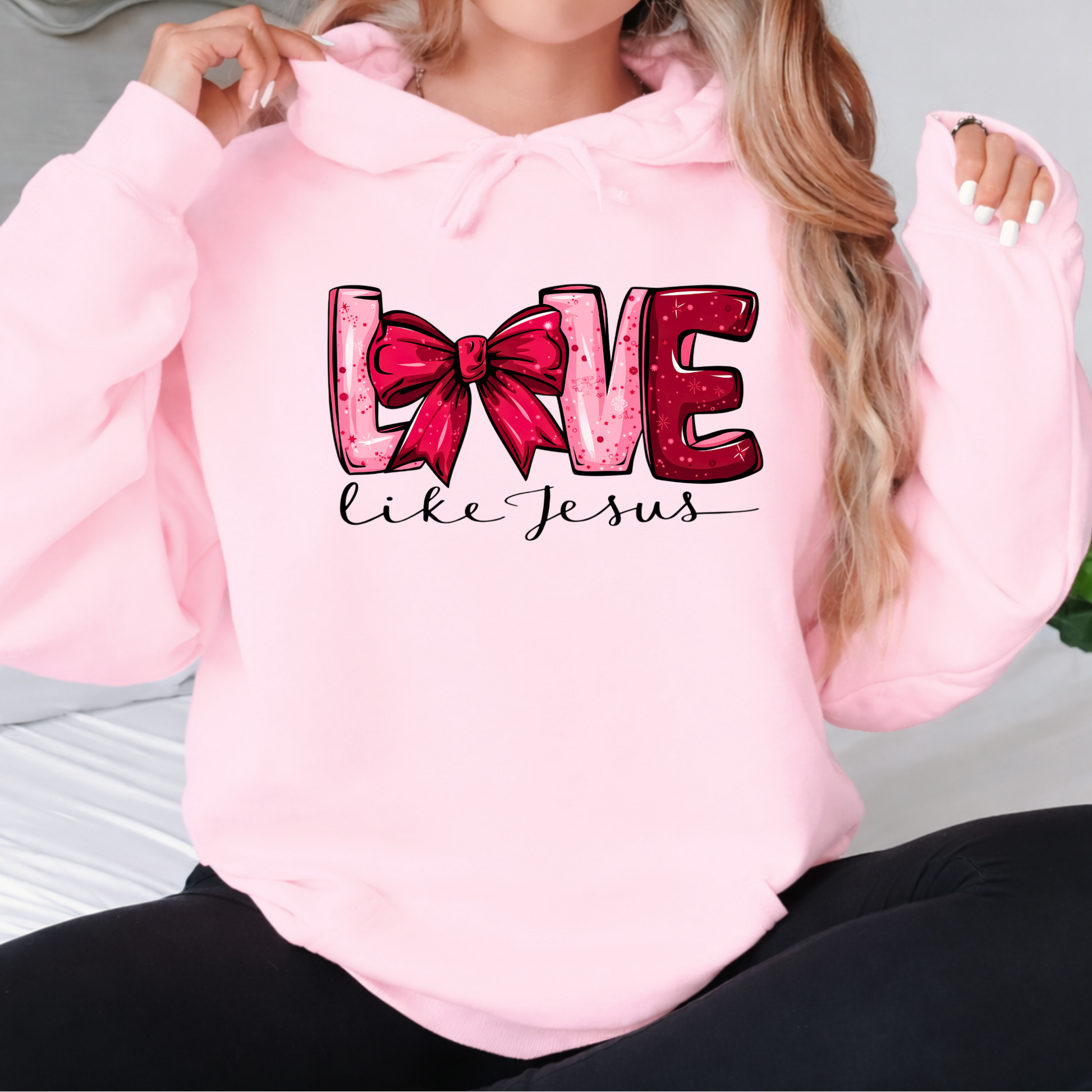 Woman wearing a Love Like Jesus light pink hoodie with pink bow graphic
