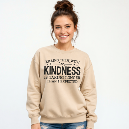 Woman modeling a sand Killing Them With Kindness crewneck sweatshirt with distressed jeans against a white background.