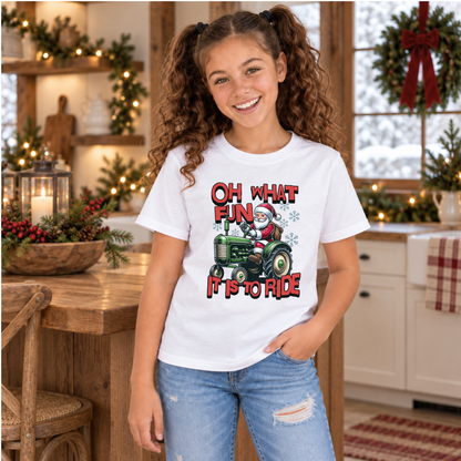 Youth white Christmas T-shirt with Oh What Fun It Is to Ride Santa tractor graphic, modeled in a decorated farmhouse kitchen