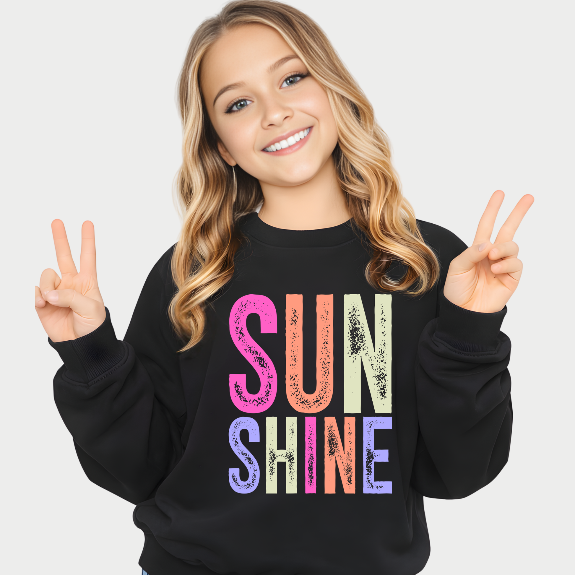 Young girl wearing a black sweatshirt with 'SUNSHINE' in colorful letters, making peace signs.