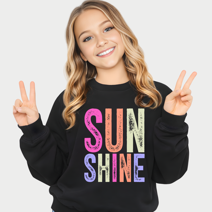 Young girl wearing a black sweatshirt with 'SUNSHINE' in colorful letters, making peace signs.