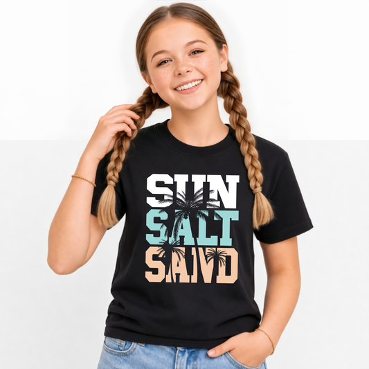 Smiling girl wearing a black youth T-shirt with a stacked Sun Salt Sand graphic in white, aqua, and peach with black palm trees.