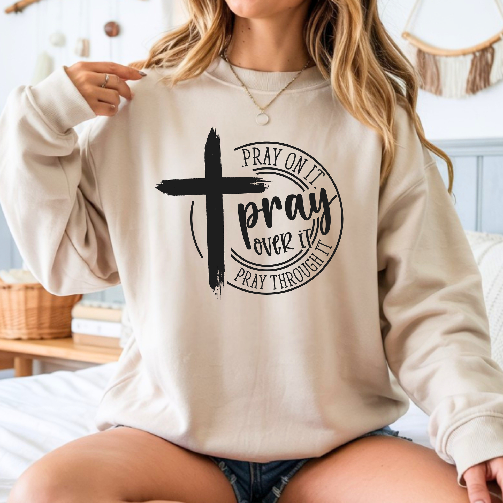 Person wearing a beige sweatshirt with a cross and text design.