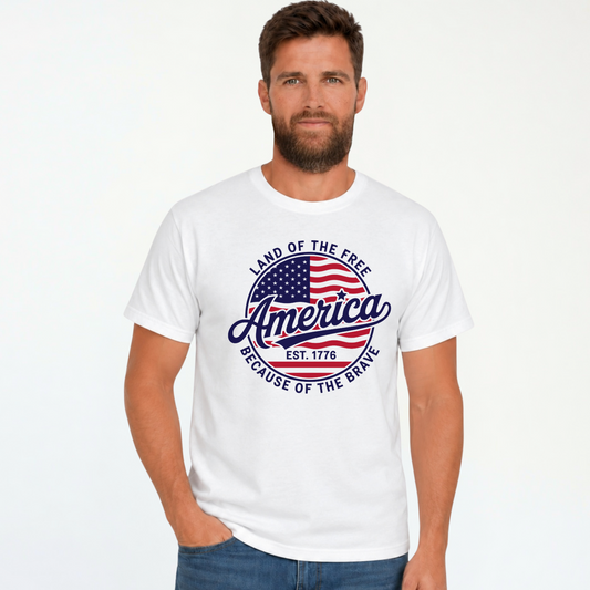Male model wearing a white T-shirt with a red, white, and blue circular America graphic reading Land of the Free, Est. 1776, and Because of the Brave.