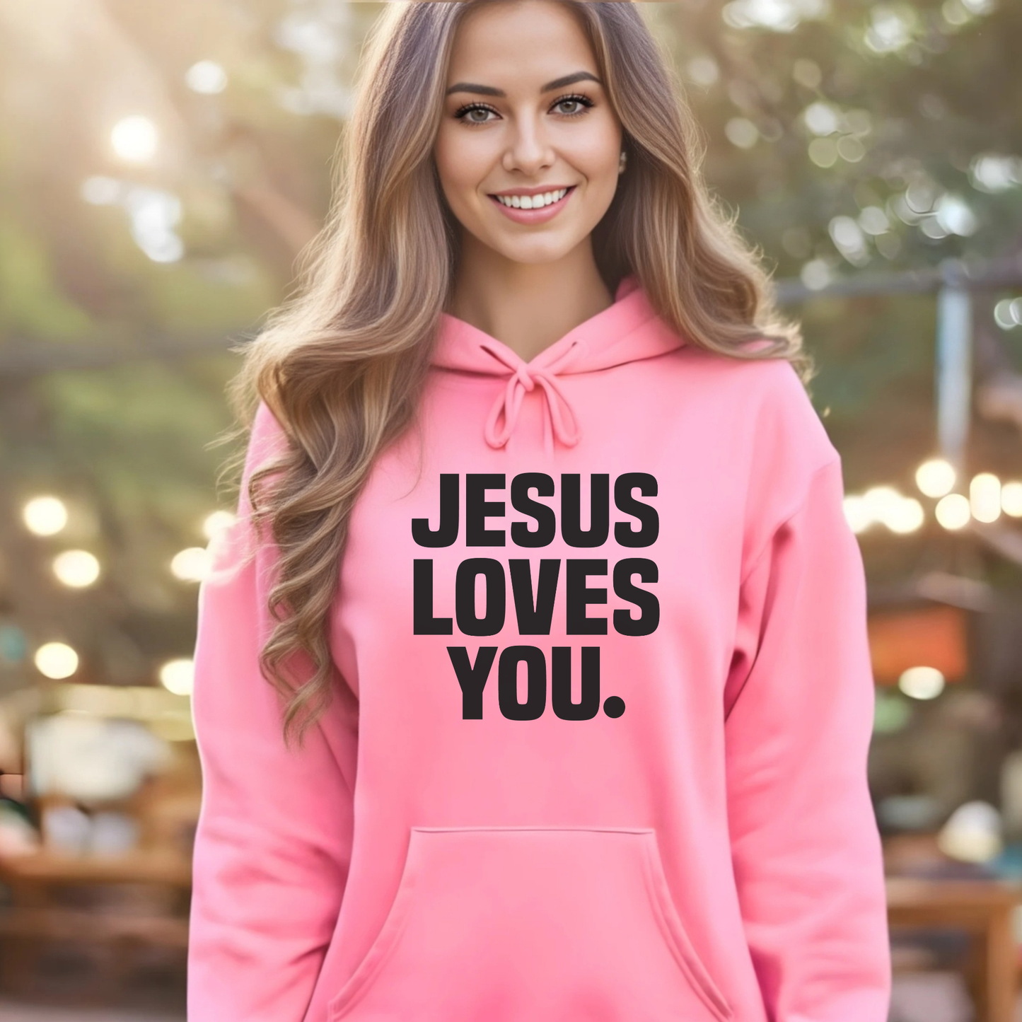 Woman wearing a pink hoodie with 'Jesus Loves You' text, standing outdoors.